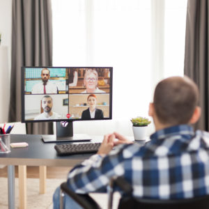 Disabled man in wheelchair during a six sigma video conference with work colleagues. Young immobilized freelancer doing his six sigma online, using high technology, sitting in his apartment, working remotely in special conditions.